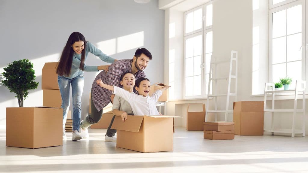 A family playing with moving boxes in the bright living room of their new home